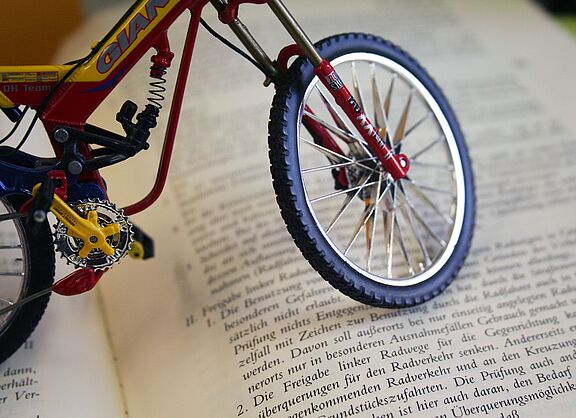 Miniatur-Fahrrad steht auf einem aufgeschlagenen Buch mit deutschem Gesetzestext.