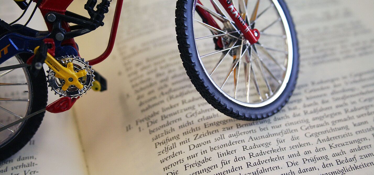 Deutscher Gesetzestext mit Fahrradbezug Miniatur-Fahrrad steht auf einem aufgeschlagenen Buch mit deutschem Gesetzestext.